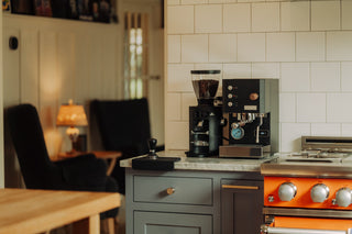 Blue espresso machine with a bean hopper on a white kitchen counter.