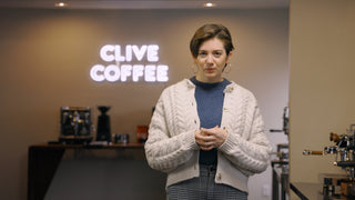 Barista in a CLIVE COFFEE shop with a glowing neon sign behind her.