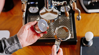 Overhead view of talent taking a Weber Workshops portafilter Unibasket out of a portafilter, lifestyle, by Clive Coffee.