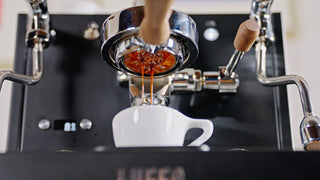 Espresso pours from the portafilter into a white cup on a professional machine.