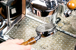 Chrome espresso machine with portafilter under the group head, water flowing into a cup on the drip tray.