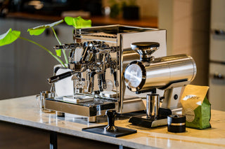 Polished dual group espresso machine on a cafe counter with cups resting on top.
