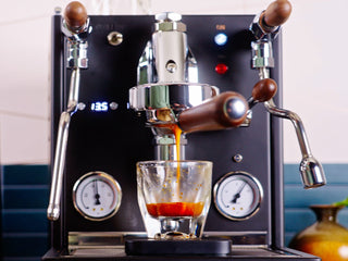 Espresso machine pouring a shot into a glass with gauges visible