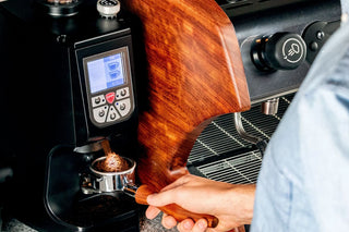 Close up of Eureka Atom 75 espresso grinder with wood side panel and a barista's hands near the portafilter.