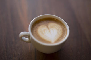 White ceramic cup of latte with a heart shaped foam design on a wooden surface.