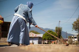 Woman in a blue denim dress and headscarf hoeing soil on a rural coffee farm