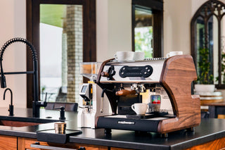 LUCCA A53 Mini espresso machine with wooden side panels and white cups on top.