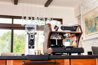 Wood trimmed espresso machine with a white cup on top and a coffee grinder beside it in a bright cafe