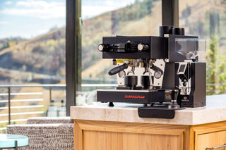 La Marzocco home espresso machine on a wooden counter with a scenic hillside view through the window