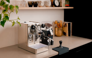 Compact home espresso setup with a black dual boiler machine on a wooden counter and a grinder nearby.
