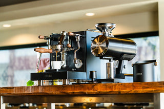 Dual group commercial espresso machine with wooden portafilter handles and a white cup nearby
