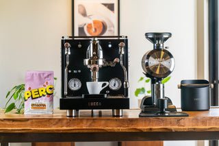 LUCCA M58 espresso machine on a wooden counter with a white cup, grinder to the right, and Ethiopian coffee bag at left.