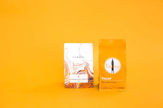 Two coffee packaging items on a bright orange background, a white marbled box on the left and an orange decaf bag on the right