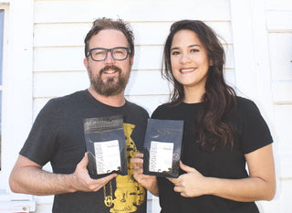 Smiling man and woman posing with bags of Panther Coffee Roasters beans.