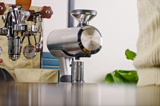 Close up of a polished espresso grinder beside a chrome espresso machine in a cafe.