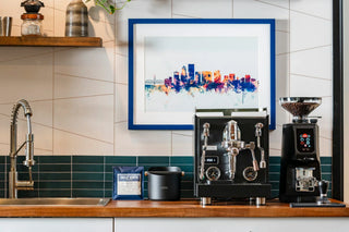 Modern home espresso station with a dual group head machine, grinder, and city skyline art on the wall