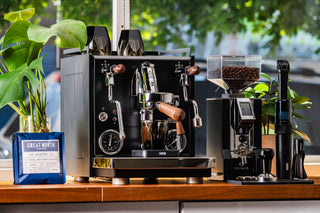 Professional LUCCA espresso machine with two groups on a counter near a bright window, with grinder and coffee gear nearby.