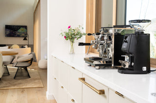 Breville espresso machine with a separate grinder on a white kitchen counter in a bright modern kitchen