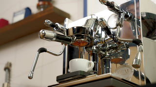 Close up of a chrome espresso machine with a portafilter and espresso dripping into a white cup