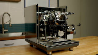 Shiny chrome espresso machine with dual group heads and gauges sits on a counter.