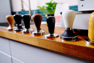 Row of espresso tampers with wooden and metal handles lined up on a wooden counter.