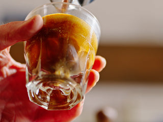 Hand holding a glass of espresso with crema on top
