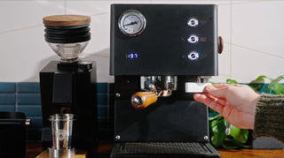 Person inserts a portafilter into a black LUCCA Tempo espresso machine in a cozy kitchen.