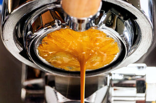 Espresso pours from a portafilter with a thick crema forming as it flows downward.