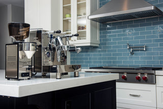 Chrome espresso station with lever machines and a blue tile backsplash in a modern kitchen.