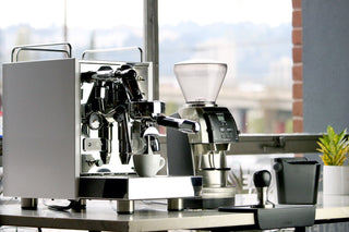 Baratza espresso machine with chrome portafilter and grinder beside a white cup on a counter