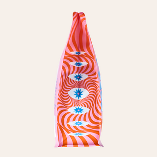 Close up of Bright Eyed Breakfast pink coffee bag showing orange swirl pattern and blue star shapes.