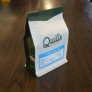 Close-up of Kenya Kiamugumo AB coffee bag with Quills Coffee label on a wooden surface