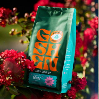 Close-up of a green Tired Eye Decaf bag with orange branding and turquoise label against a vibrant floral backdrop.