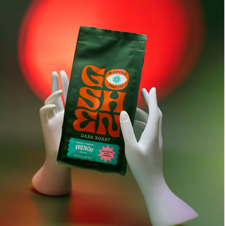 Heavy Feels French dark roast bag held by white hands with a colorful blurred background