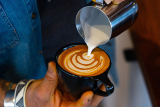 Hand pours steamed milk into a cup to create latte art swirls