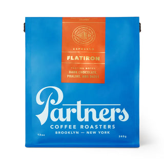 Bright blue Partners Coffee Flatiron espresso bag with orange label listing tasting notes dark chocolate praline and dates.