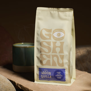 Close up of a white PERU ABDON QUILLA OCHOCHOQUE coffee bag with a beige logo against a dark background