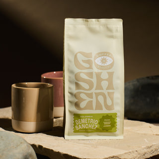 Colombia Demetrio Sanchez Gesha coffee bag standing upright on a counter with mugs in the blurred background.