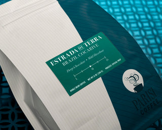 Estrada de Terra coffee packaging with teal label on a blue striped surface beside notebook pages.