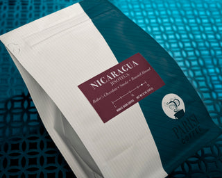 Nicaragua Jinotega coffee bag with maroon label resting on a notebook against a teal backdrop.