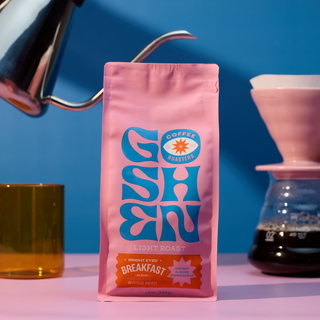 Bright Eyed Breakfast pink coffee bag with light roast label and Goshen Coffee Roasters logo set against a blue background.