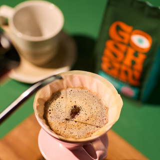 Espresso with crema in a white cup with a brown paper filter nearby on a green surface.