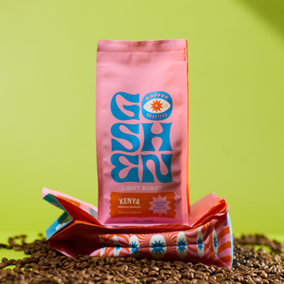 Pink Mbegu Ndogo Kenya whole bean coffee bag with orange Kenya label amid coffee beans on a bright backdrop.