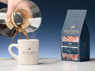 Pouring coffee from a carafe into a white Kaldi's Coffee mug next to the 700 bag.
