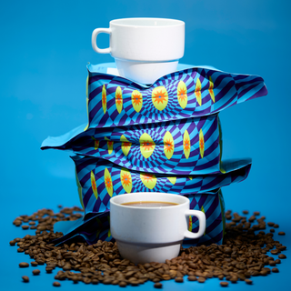 White ceramic mug balanced atop a colorful wrapped coffee bag against a blue background.