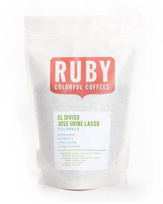 White coffee bag with a large Ruby logo and El Diviso Jose Uribe Lasso Colombia label listing pomegranate strawberry creme brulee orange blossom.