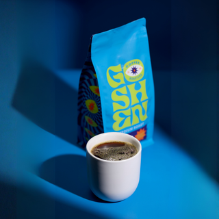 White mug of coffee in front with a blue Guatemala Cachito Whole Bean bag in the background.