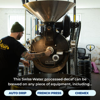 Worker in a green beanie operates a Probat coffee roaster in a workshop for Ghost Town Decaf.