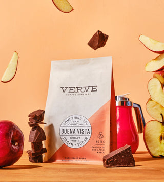 Buena Vista Verve coffee bag held against a peach backdrop with sliced apples and chocolate chunks nearby.