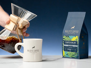 Pour-over coffee pours from a glass carafe into a white Kaldi's mug beside a Cafe Kaldi bag.
